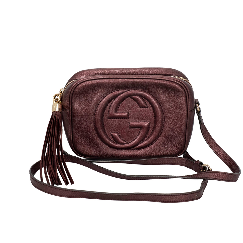 Gucci Metallic Pebbled Calfskin Small Soho Disco Bag in a rich burgundy/purple metallic hue with the signature embossed interlocking GG logo on the front and a bold matching leather tassel zipper pull.