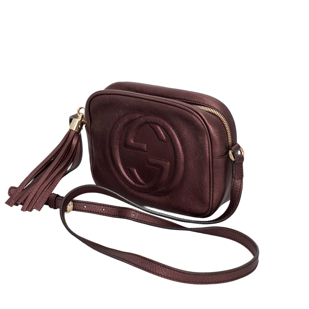 Gucci Metallic Pebbled Calfskin Small Soho Disco Bag in a rich burgundy/purple metallic hue with the signature embossed interlocking GG logo on the front and a bold matching leather tassel zipper pull.