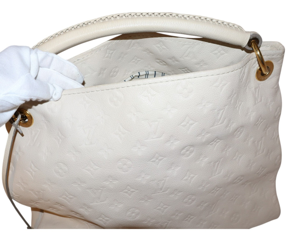 front view Louis Vuitton white embossed monogram leather handbag with a top handle, shown with a white gloved hand holding the opening. The bag features gold-tone hardware and is set against a plain white background.