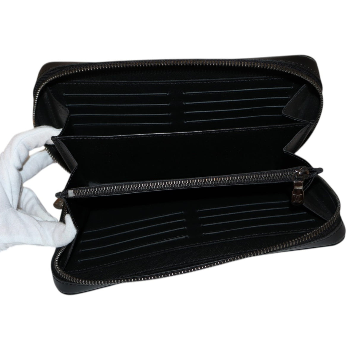 interior view Louis Vuitton open black leather zip-around wallet with multiple card slots and compartments, held open by a white gloved hand against a plain white background.