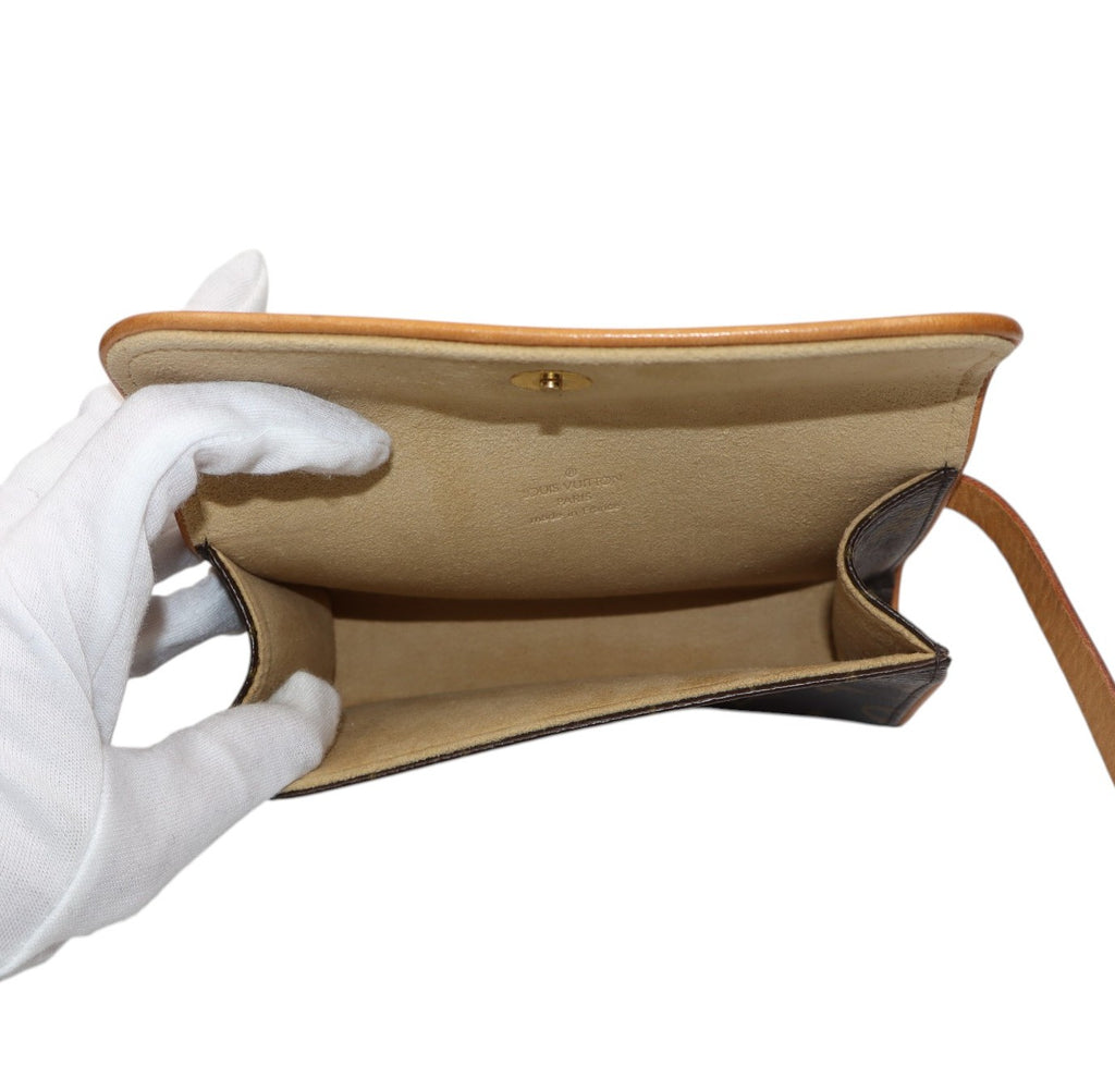 A hand wearing a white glove holds open a vintage Louis Vuitton pochette to show the interior. The belt bag style bag has a tan leather exterior, a beige canvas lining, and a small gold-tone snap button closure.