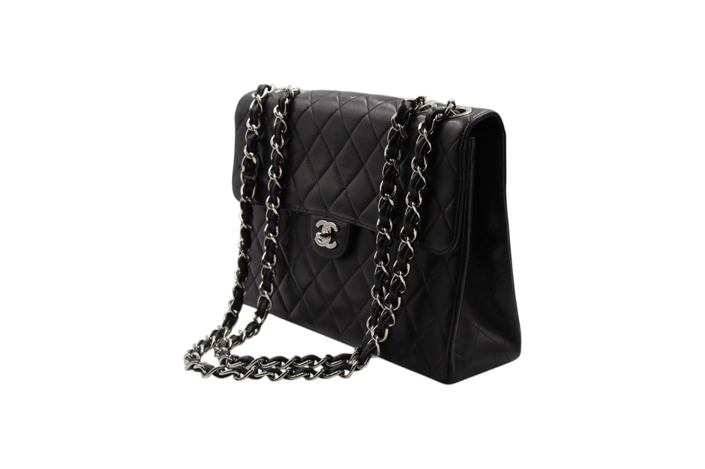 diagonal view Chanel black quilted leather shoulder bag with silver-tone chain straps and a silver interlocking CC logo on the front, photographed on a plain white background.
