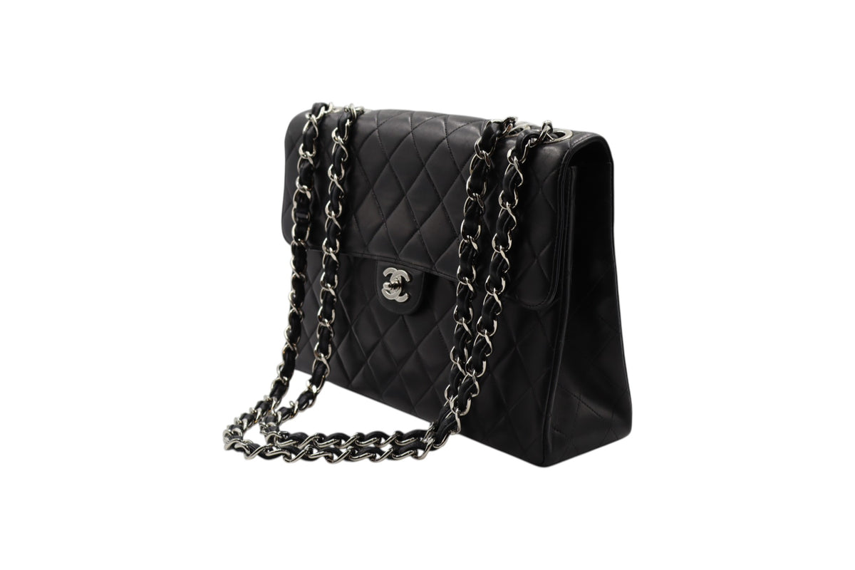 diagonal view Chanel black quilted leather shoulder bag with silver-tone chain straps and a silver interlocking CC logo on the front, photographed on a plain white background.