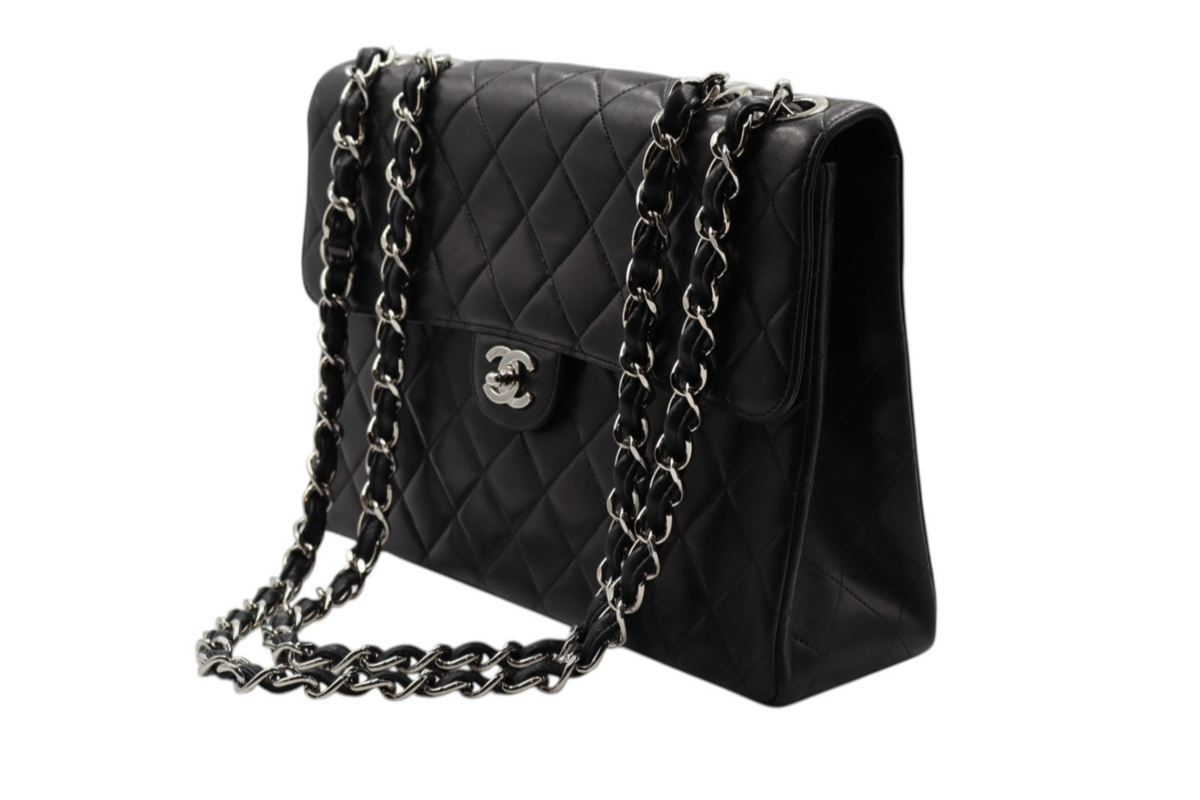 diagonal view Chanel black quilted leather shoulder bag with silver-tone chain straps and a silver interlocking CC logo on the front.