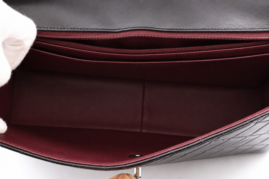 Close-up of the interior of Chanel black quilted leather handbag, showing a deep burgundy-red lining with zippered compartments and a smooth fabric insert.