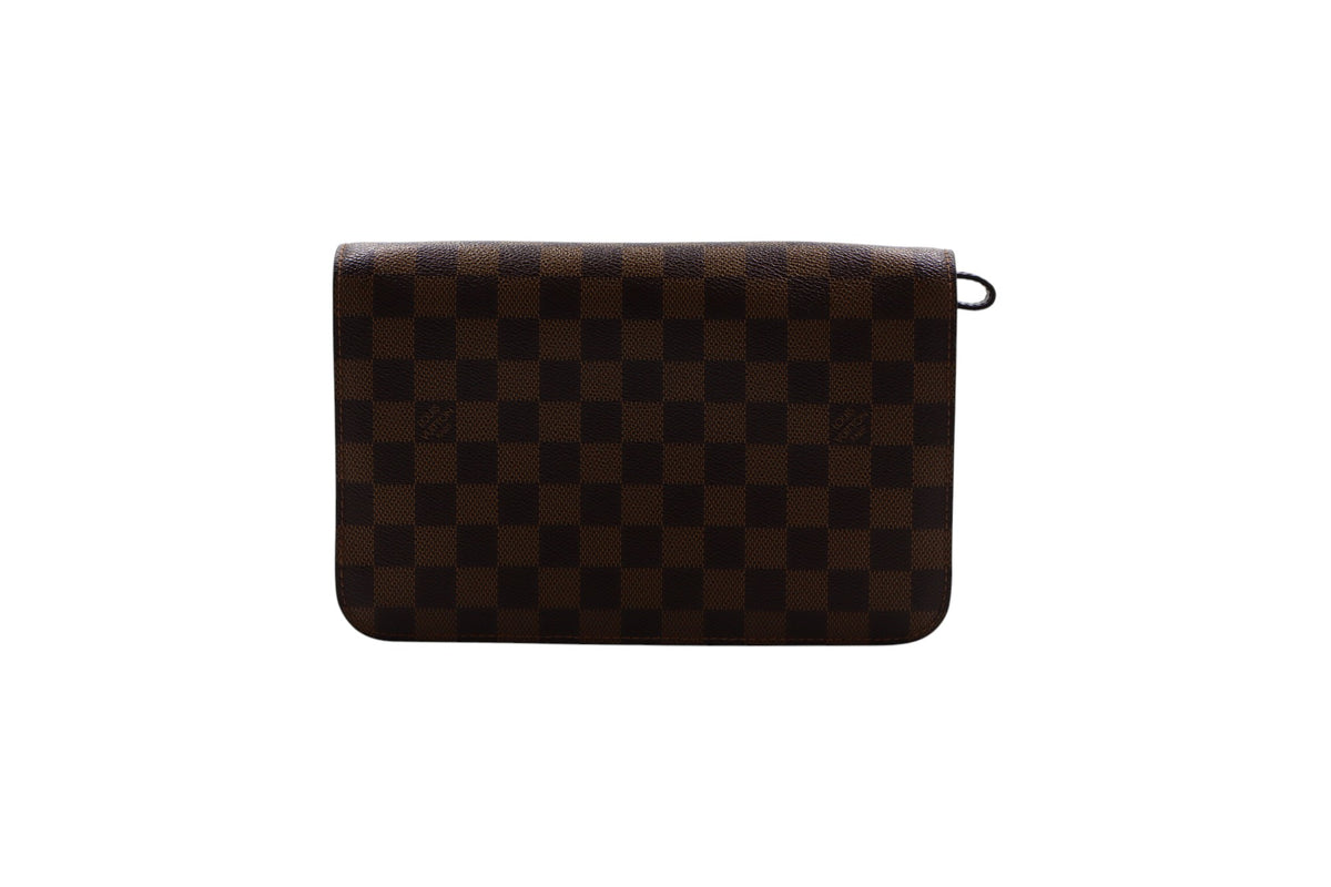back view of a Louis Vuitton brown and black checkered clutch bag with a small black ring detail on the right side, set against a plain white background.