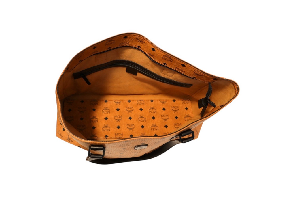 Inside view of MCM orange Visetos tote bag with black monogram print, inside zipper pocket, black leather shoulder straps, and an open-top design on a white background.