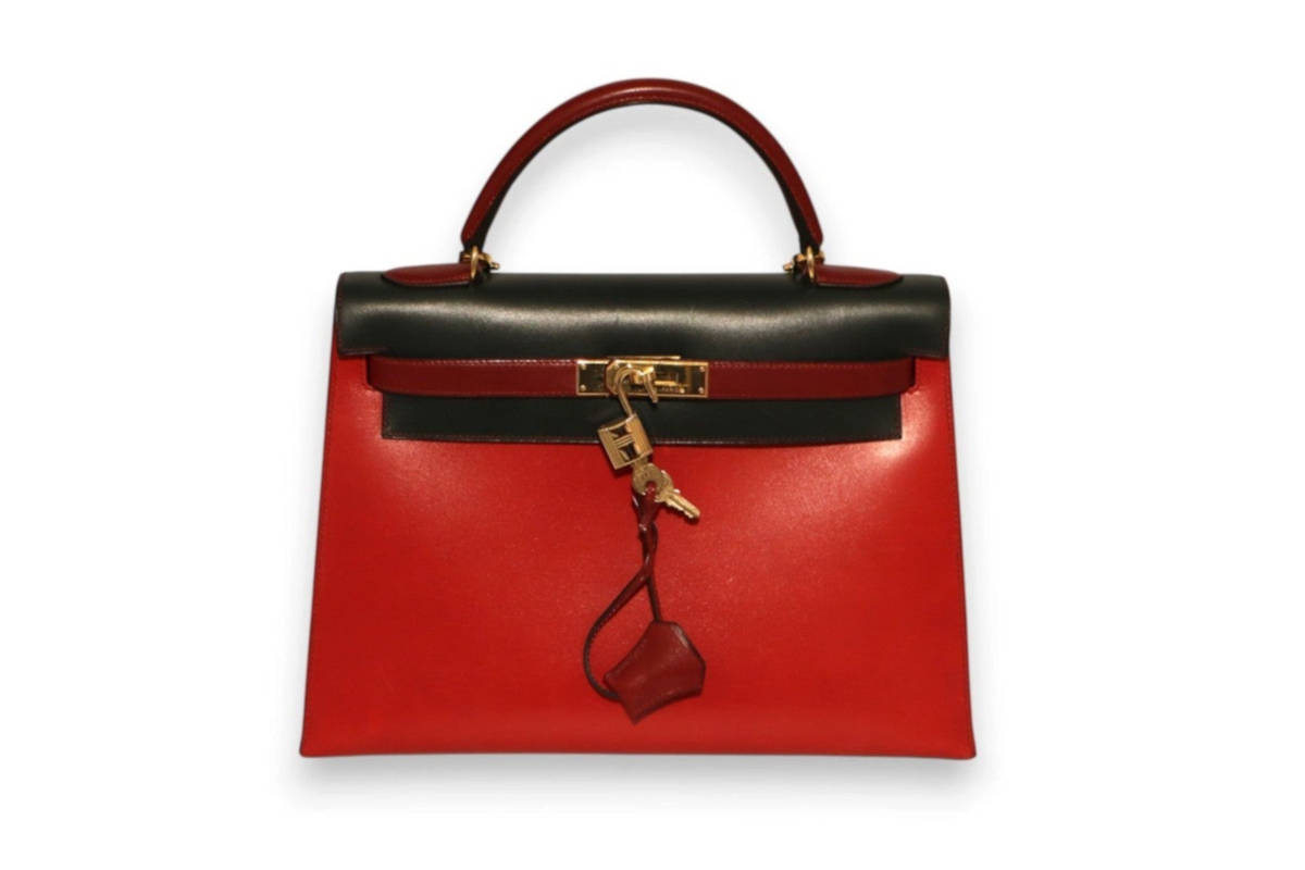 A structured Hermes red leather handbag with a black top handle and trim, gold-tone hardware, and a hanging clochette.
