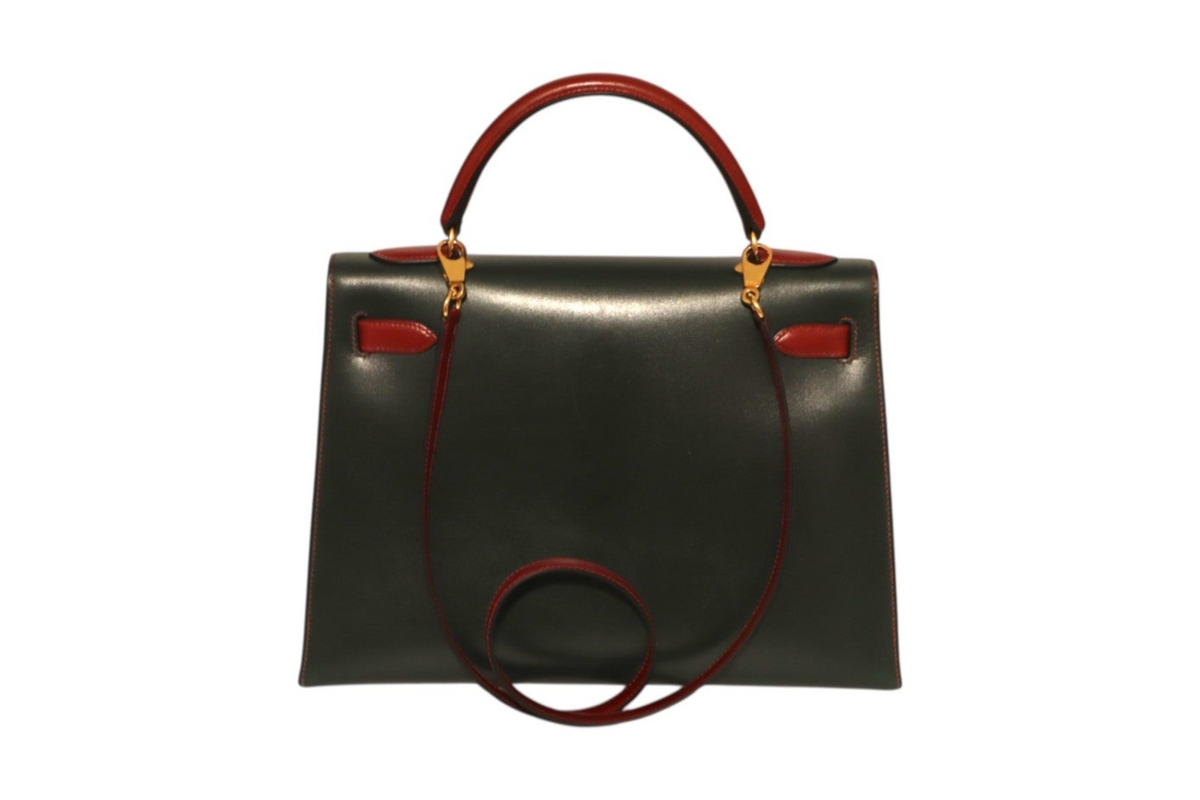 A structured Hermes black leather handbag with a top handle and shoulder strap in a deep burgundy red, accented by gold-tone hardware and small red leather tabs on the front.