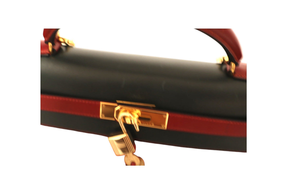 Close-up of a structured Hermes handbag with a black leather body, red leather trim, and gold-tone hardware.