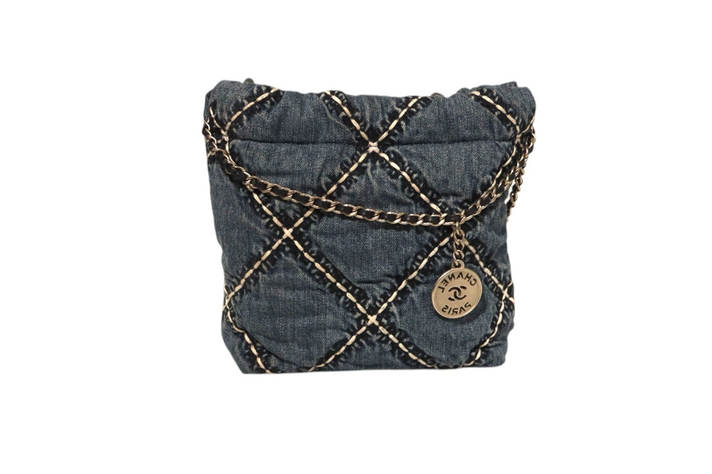 Back view of Chanel dark denim quilted drawstring bucket bag with contrasting stitching, gold-tone chain detailing, and round Chanel Paris CC logo charm on a white background.