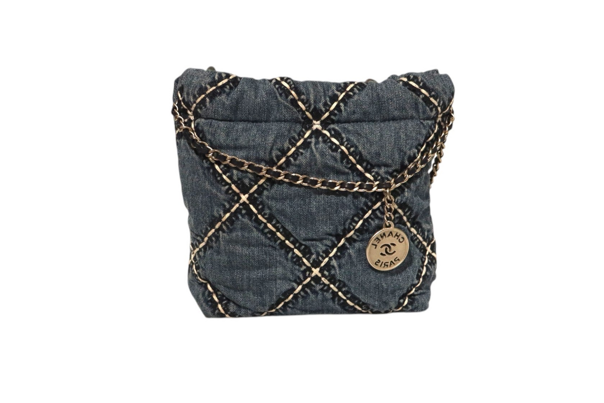 Back view of Chanel dark denim quilted drawstring bucket bag with contrasting stitching, gold-tone chain detailing, and round Chanel Paris CC logo charm on a white background.