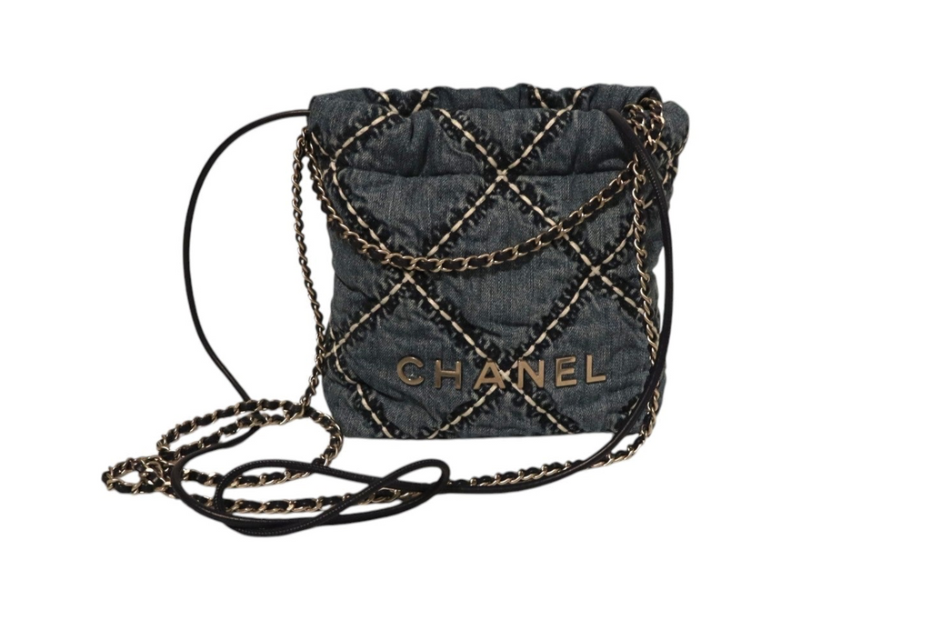 Front view of Chanel dark denim quilted drawstring bucket bag with gold-tone chain detailing, CHANEL logo lettering, and long black leather and chain shoulder strap on a white background.