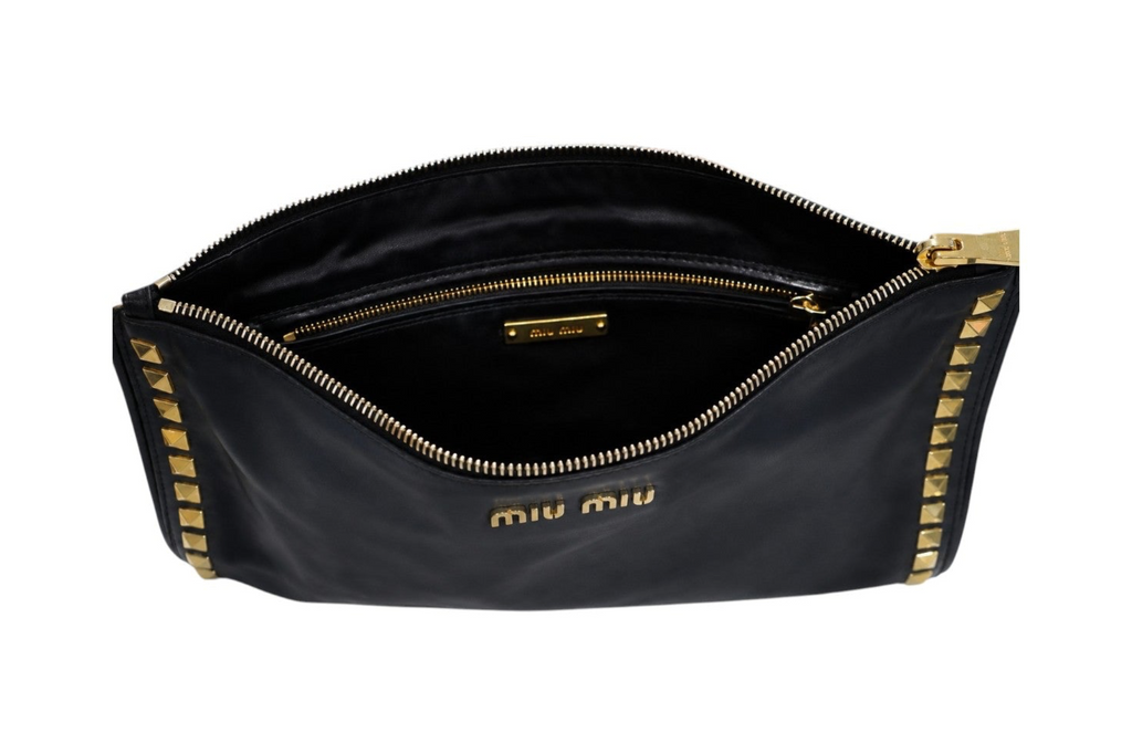 A black Miu Miu nylon pouch bag shown open, featuring gold-tone hardware, a gold zipper, and gold studs along the edges, with the 'miu miu' logo printed in gold on the front.