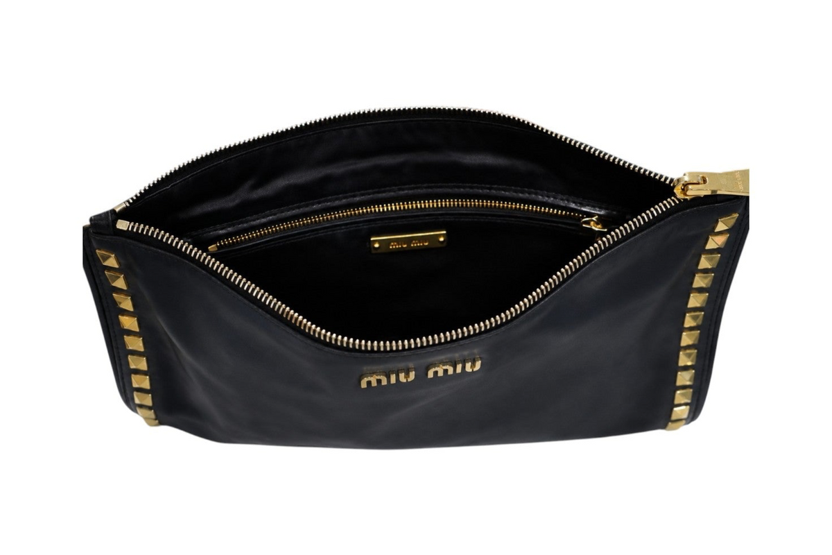 A black Miu Miu nylon pouch bag shown open, featuring gold-tone hardware, a gold zipper, and gold studs along the edges, with the 'miu miu' logo printed in gold on the front.