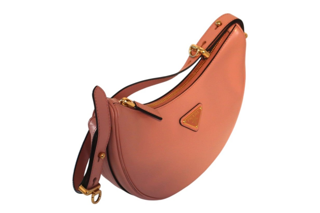 A crescent-shaped pink Prada leather shoulder bag, featuring gold-tone hardware and a small triangular metal logo plaque.