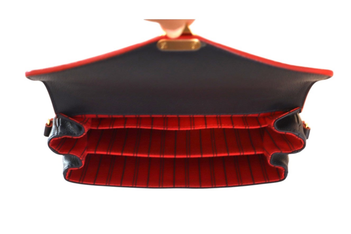 A structured Louis Vuitton navy leather shoulder bag shown open from a top-down view, featuring a black exterior with red piping and a red-and-black vertically striped interior.